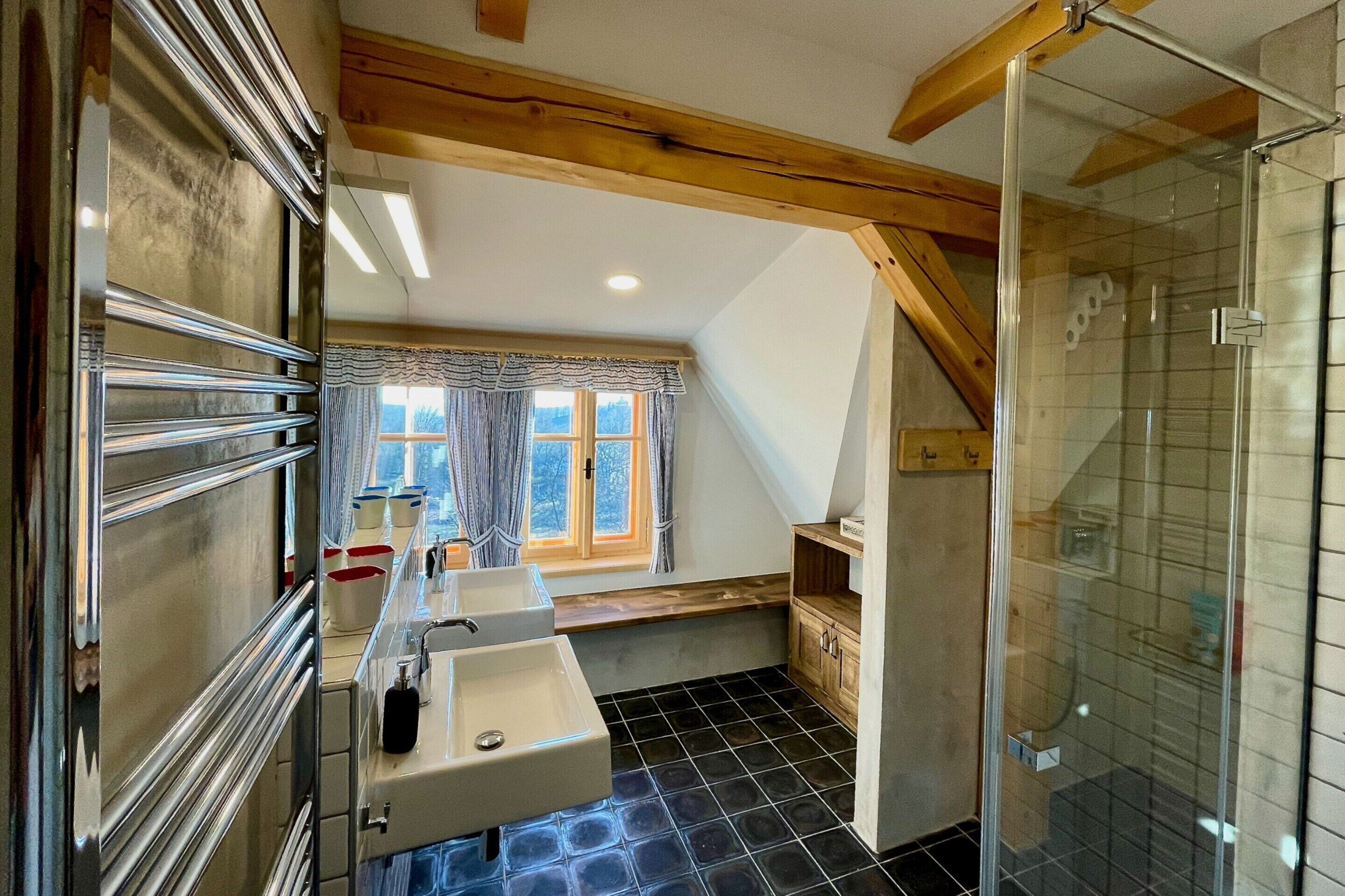 A bathroom with a shower, two sinks, and a window with curtains.