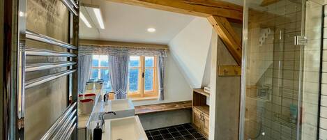 A bathroom with a shower, two sinks, and a window with curtains.