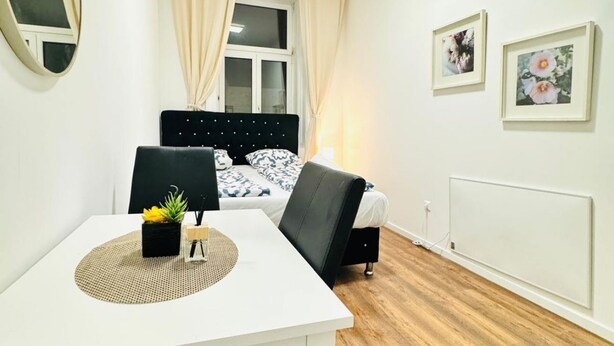 A bedroom with a bed, a bedside table with a plant, a chair, and a window with curtains. - Comfortable Room for 2, Close to Atzgersdorf (Vienna)
