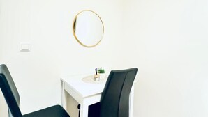 Une pièce avec deux chaises noires, une table blanche, une petite plante en pot et un miroir rond accroché au mur.