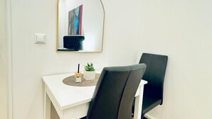 A room with a white desk, two black chairs, a small potted plant, a wall-mounted mirror, and a light switch. - Convenient Stay Room for 2, 11 Min to Atzgersdorf (Vienna)