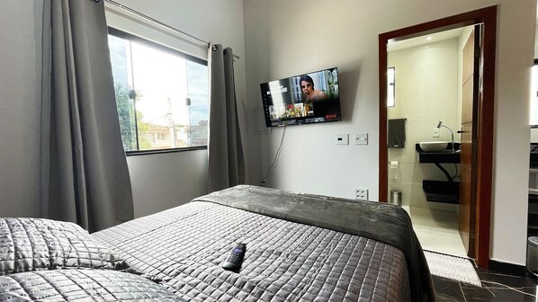 A hotel room with a bed, a TV mounted on the wall, and a bathroom visible through an open door.