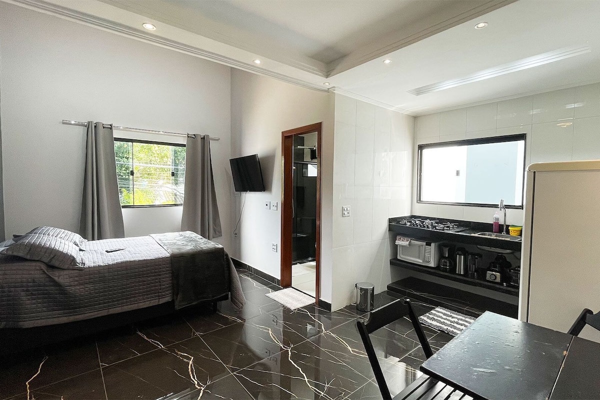 A compact room with a bed, a small kitchenette, a dining area, and a TV mounted on the wall.
