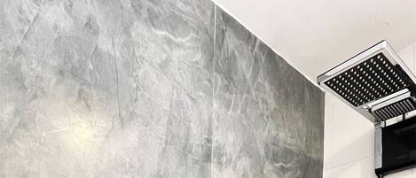 Une salle de bain avec de grandes carreaux de marbre gris, deux vasques rectangulaires noires et une bouche d’aération au plafond.