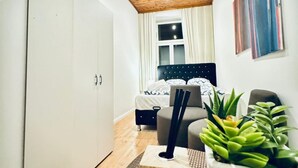 Un dormitorio con cama, armario, planta y ventana con cortinas.