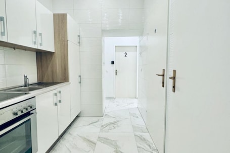A narrow kitchen with white cabinets, a stainless steel sink, and a marble floor.