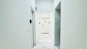 Un couloir étroit aux murs blancs et au sol en marbre mène à une porte portant le numéro 4.