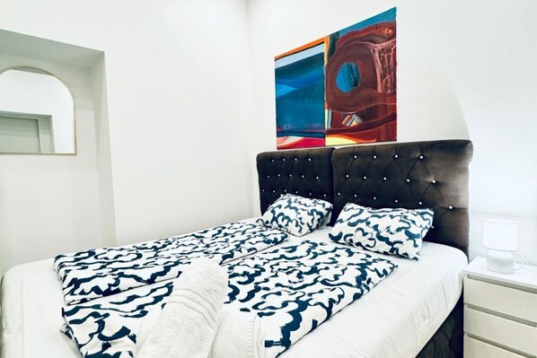 A neatly made bed with patterned bedding, a tufted headboard, and a bedside table with a lamp.