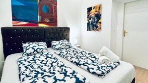 Un lit double avec une couvre-lit à motifs, une tête de lit capitonnée et deux tableaux accrochés au mur.