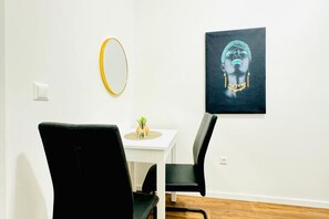 A room with a white wall, a round mirror, a black chair, a white table, and a framed artwork.