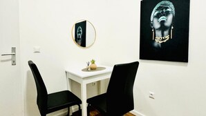 A room with a white wall, a round mirror, a black and white painting, a small table with a plant, and two black chairs. - Beautiful Room Close to Atzgersdorf (Vienna)