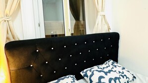 A bed with a tufted headboard, two patterned pillows, and a window with curtains.
