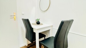 A small room with a white table, two chairs, a round mirror, and a small potted plant.