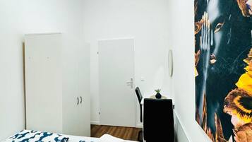 Ein Schlafzimmer mit Bett, Tür, Sessel, einem kleinen Tisch mit Pflanze und einem großen abstrakten Gemälde an der Wand.