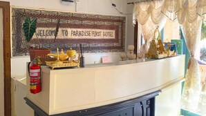 Et receptionsområde med et skilt der siger 'Welcome to Paradise First Hotel', en lysekrone og en brandslukker.