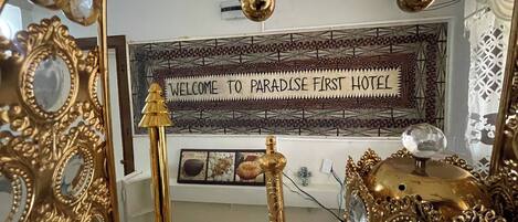 A sign reading 'WELCOME TO PARADISE FIRST HOTEL' with ornate gold-framed mirrors and decorative elements.