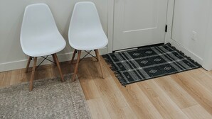 A room with a white door, two white chairs, a patterned rug, and a textured rug on the floor. - Cozy Casita (Price)