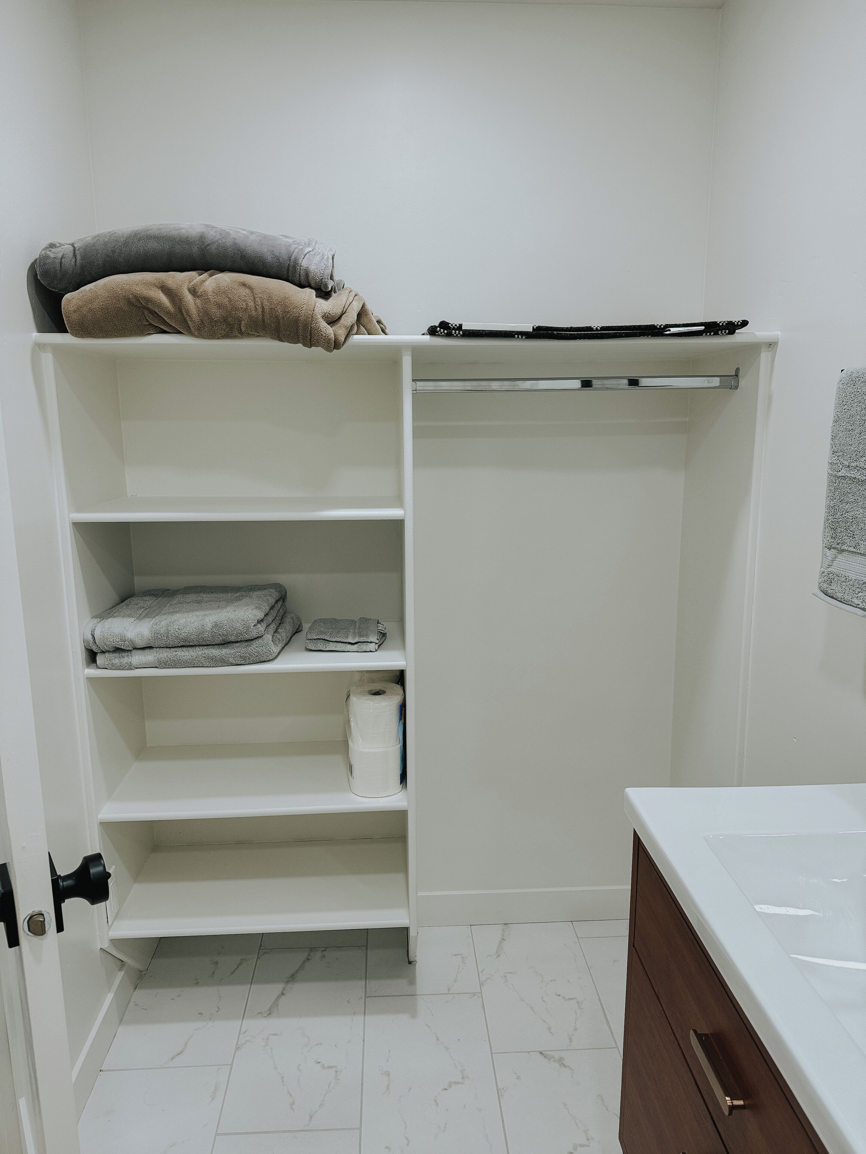 Un dressing avec des étagères, une tringle à vêtements et un porte-rouleau de papier toilette.