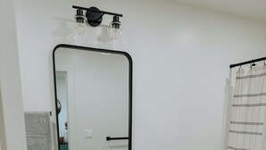 A bathroom with a white sink, wooden vanity, a mirror, a toilet, and a shower curtain. - Cozy Casita (Price)
