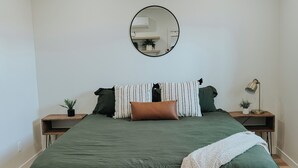 A bedroom with a large bed, a round mirror on the wall, and two bedside tables with lamps. - Cozy Casita (Price)