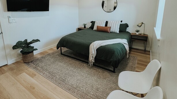A modern bedroom with a bed, a TV, a mirror, and a window. - Cozy Casita (Price)