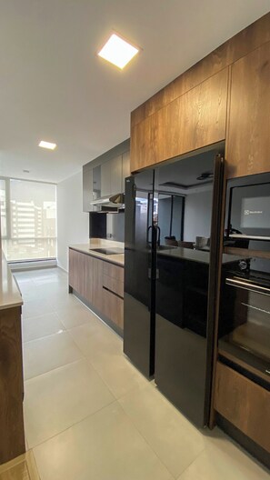 A modern kitchen with wooden cabinets, a black refrigerator, and a built-in oven.