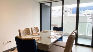 A modern dining room with a large table, cushioned chairs, and a view of the city through large windows.