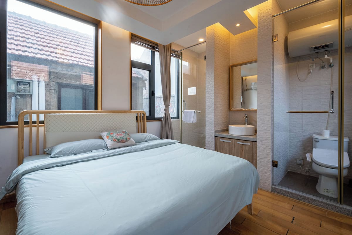 Habitación de hotel con cama, baño con ducha y vistas al exterior.