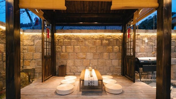 Un área de comedor al aire libre con un fondo de pared de piedra, una pérgola de madera y una parrilla.