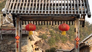 Una estructura arquitectónica china tradicional con techo de madera, escalones de piedra y dos estatuas de leones de piedra en la entrada.