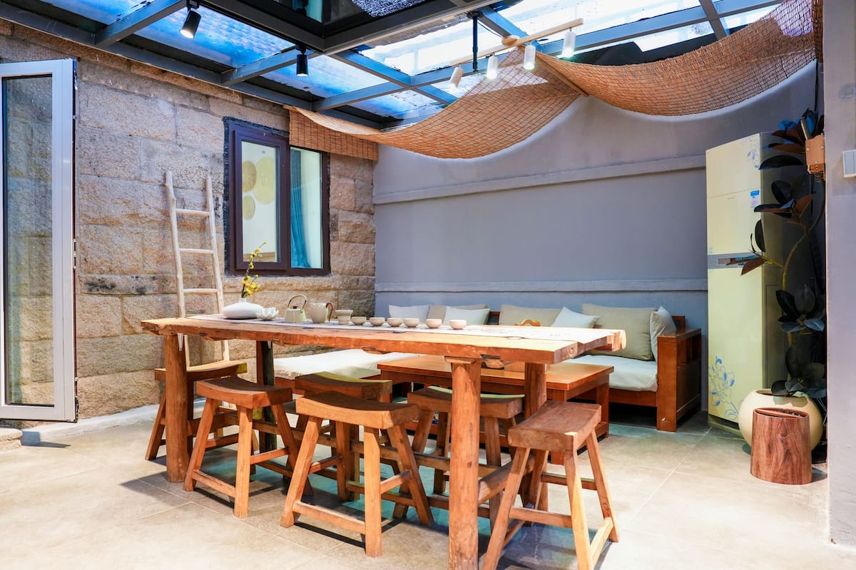 Un espacio comedor al aire libre rústico con pared de piedra, muebles de madera y una hamaca.