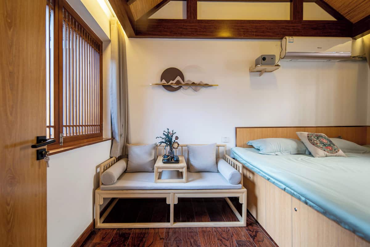 Una habitación con un banco de madera, una cama con almohadas y un equipo de aire acondicionado en la pared.