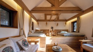 Una habitación acogedora y luminosa con vigas de madera, un sofá con cojines estampados, una mesita con un cuenco y una cama con cabecero.