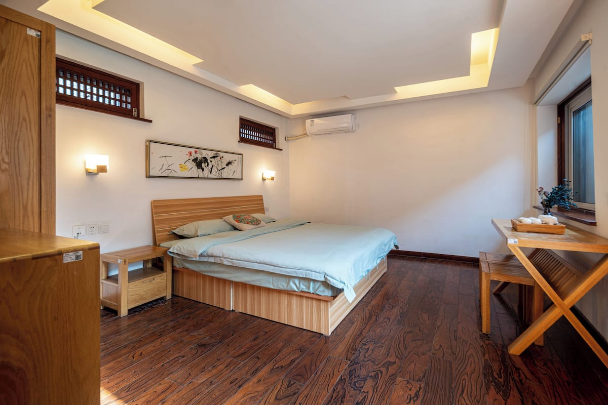 Un dormitorio moderno con una cama de madera, mesitas de noche, un escritorio y un ventanal grande.