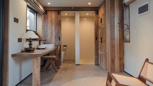Un pasillo con un escritorio de madera, una silla y una lámpara, que conduce a un baño con inodoro y lavamanos.