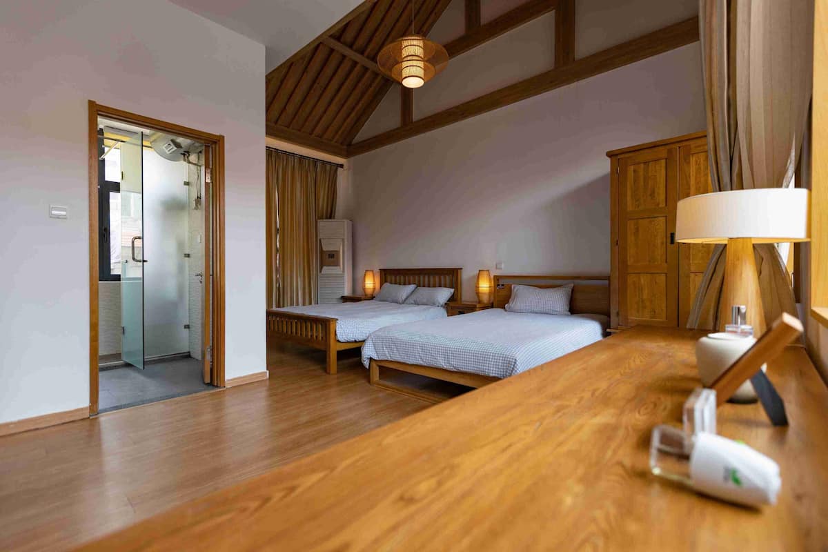 Un dormitorio con dos camas, pisos de madera, techo de madera y una mesita de noche con lámpara.