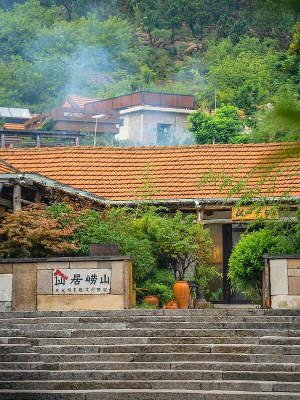 Un bâtiment japonais traditionnel, avec un toit recouvert de tuiles, des marches en pierre menant à l’entrée et une enseigne portant des caractères japonais.