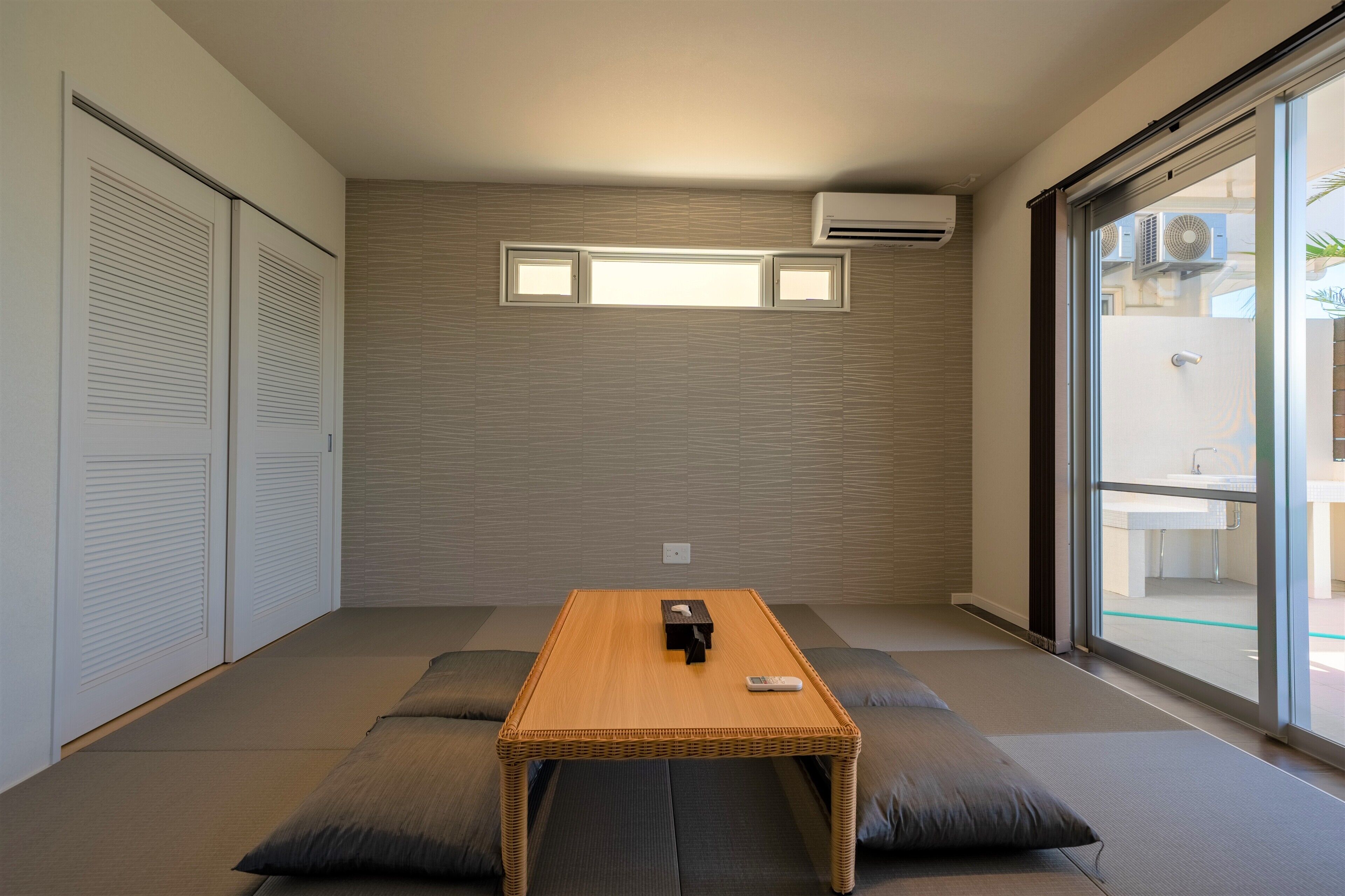 A room with a tatami mat floor, a low wooden table, and a sliding glass door leading to an outdoor area.