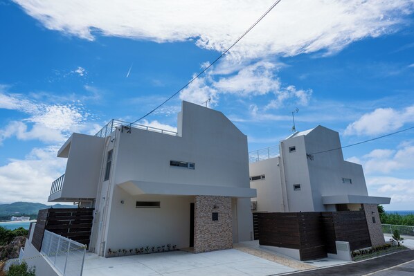 A modern two-story house with a balcony, a stone facade, and a view of the sea.