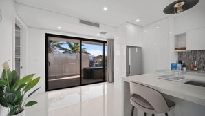 Eine moderne Küche mit einer großen Kochinsel, einem Kühlschrank und einer Schiebetür zu einer Terrasse.
