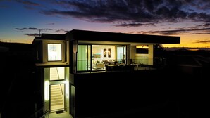 Ein modernes Haus mit Glasfassade, einer sichtbaren Treppe und einem Balkon.