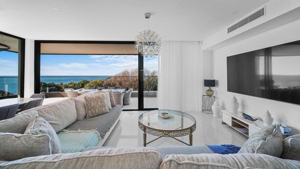 Ein modernes Wohnzimmer mit großem Fernseher, bequemen Sitzmöglichkeiten und Blick aufs Meer.
