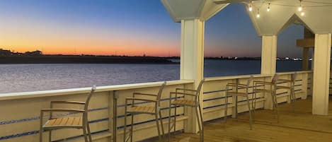 A wooden deck with chairs and a railing overlooking a body of water at dusk.