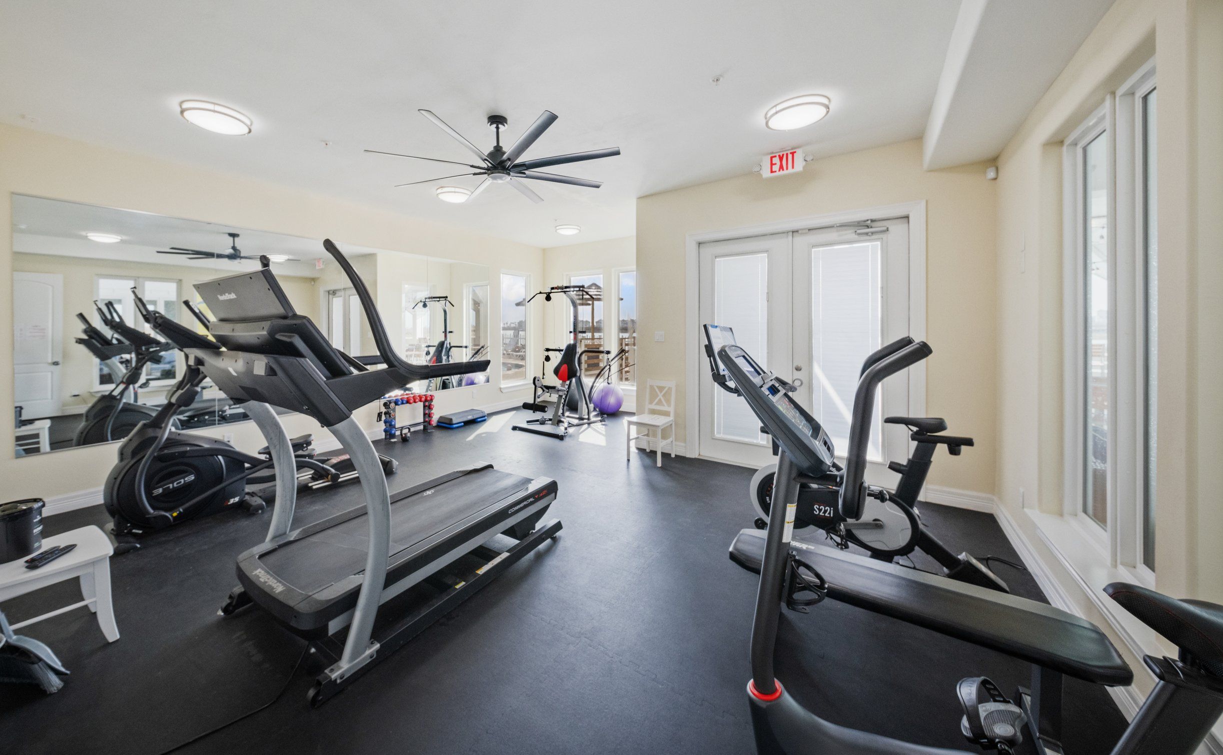 A gym with treadmills, elliptical machines, and a ceiling fan.