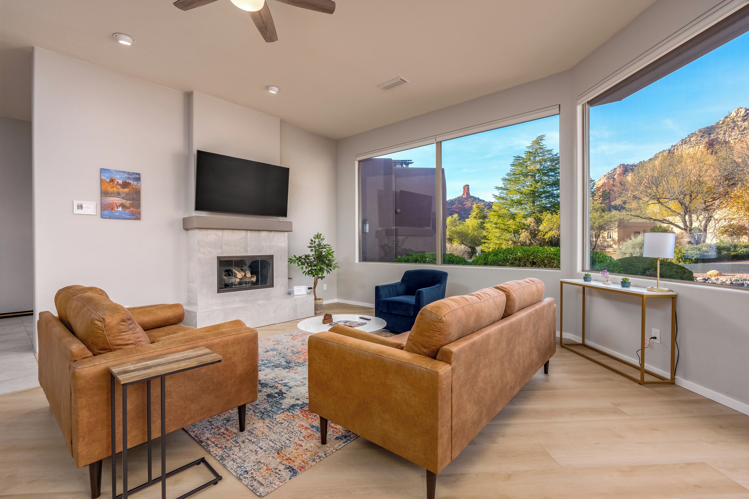 A modern living room with a fireplace, leather sofas, a coffee table, and a large window offering a view of trees and mountains.