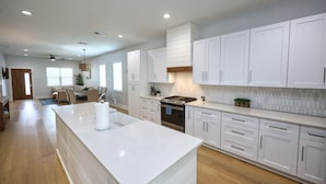 A spacious kitchen with white cabinets, a large island, and a built-in oven. - Modern Lux Home 2 Mins to the Beach+Putting Green
 (Galveston)