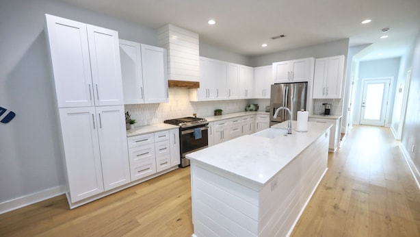 A modern kitchen with white cabinetry, a large island, and a stainless steel refrigerator. - Modern Lux Home 2 Mins to the Beach+Putting Green
 (Galveston)