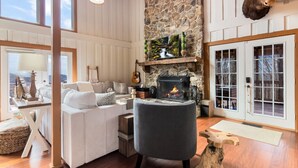 A cozy living room with a fireplace, a stone wall, and a mounted moose head. - King Bed, Arcade, Hot Tub, Amazing Views (Jasper)