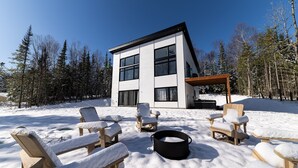 Een modern herenhuis met een patio, voorzien van houten stoelen en een zwarte pot.