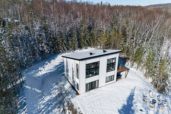 A modern, two-story cabin surrounded by a snowy forest. - Au Clair de Lune 103: River View, Hot Tub & Trails (Les Éboulements)